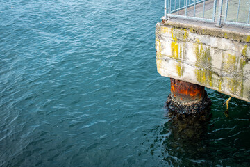 Aged pier with algae and rust details over calm blue sea water, concrete pier with rusted support...