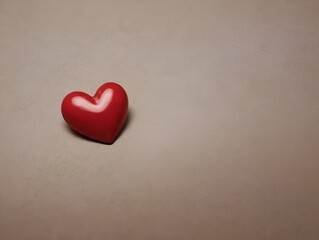 Fototapeta premium a small, red, heart-shaped object placed on a plain, light-colored surface. The heart has a smooth texture and a slight shine, suggesting it might be made of plastic or a similar material