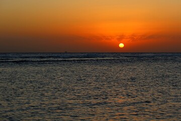 Vivid rising morning sun, calm water surface under the clouds. Distant dark sky, water and colorful sunrise. Dawn by the ocean, travel landscape photography. 