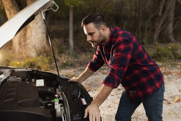 Man looking at open hood of broken car on road