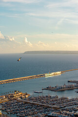 A stunning aerial view of a marina filled with boats and yachts, with a long pier extending into the calm sea under a beautiful sunset sky. Alicante, Spain.