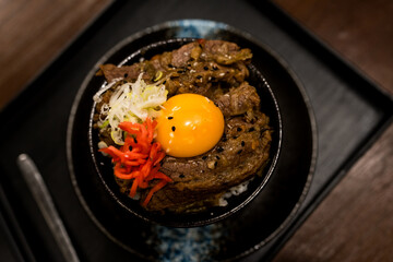 Roast Wagyu beef rice and raw egg bowl, the creamy yolk embrace the succulent beef, blending into a delectable harmony of textures and flavors in a black bowl.