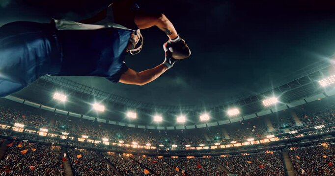 This video captures a dramatic moment in an American football game as a player in a blue jersey dives mid-air to catch the ball. The bright stadium lights and cheering crowd amplify the intensity and 