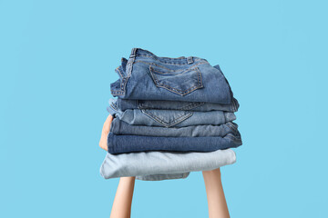Female hands with stack of different jeans on blue background