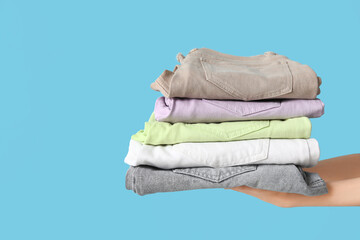 Female hands with stack of jeans on blue background