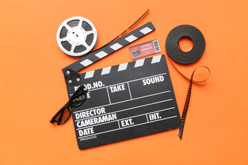 Movie clapper with film reels, cinema ticket and glasses on orange background