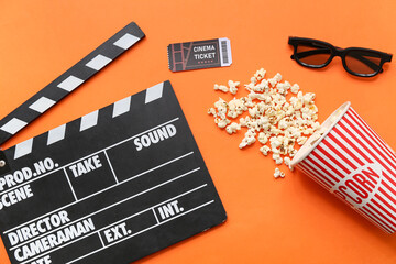 Movie clapper with cinema ticket, glasses and popcorn on orange background