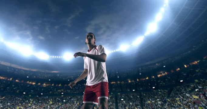 Football player, wearing red and white uniform, receives the pass and kicks the ball in slow motion on the professional football stadium with animated crowd.