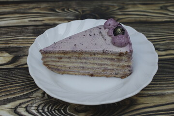 Closeup of a piece of Mille Crepes with blueberry cheesecake flavor on a small white plate on the wooden table.