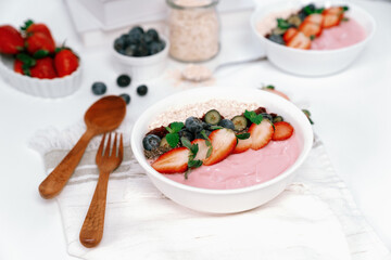 Presented by fruits putting yogurt toppings with strawberry, berry, oats, raisins and chia seed decorated by peppermint in white blow. Pink background. Set of healthy dairy product choice. Pecuniary.