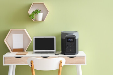 Portable power station with laptop on table near green wall in office