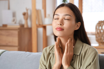 Young Asian woman self-examining thyroid gland at home, closeup