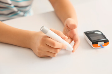 Diabetic girl using lancet pen at table in clinic, closeup