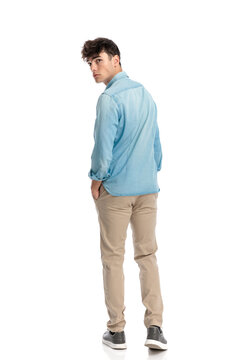 young casual man with hands in pockets looking behind over shoulder
