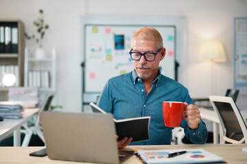 Fototapeta premium Focused businessman enjoying a cup of coffee while reviewing notes in a modern office