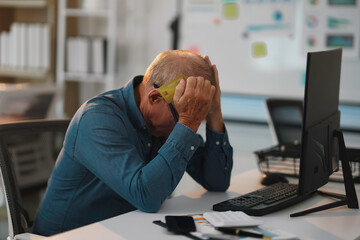 Desperate mature man sitting at office desk with head in hands, holding credit card and having...