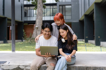 Three happy students collaborating on a project using a laptop, enjoying teamwork and online learning outdoors