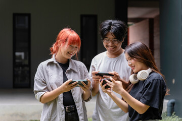 Three happy asian friends are using smartphones, enjoying mobile gaming together outdoors
