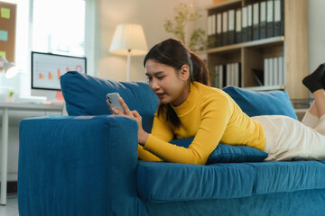 Asian businesswoman using smartphone while lying on sofa in home office, working from home concept