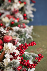 Christmas garland with pine needles, white branches and red decorations on a blue background