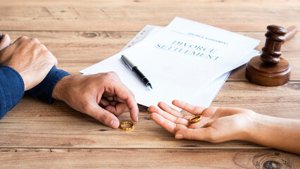 Human hand signing divorce contract, close-up. Wedding rings with marriage contract and judge gavel on a  background