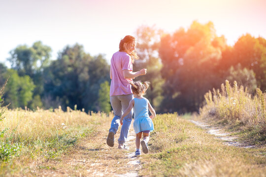 Happy mother walking with little daughter outdoors in summer. The mother and kid run in the field. Happy childhood, family, and Mother's Day concept