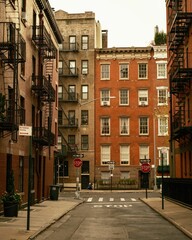 A quiet intersection surrounded by brick buildings and fire escapes with stop signs and a one-way street in Gay Street, West Village, Manhattan, New York.