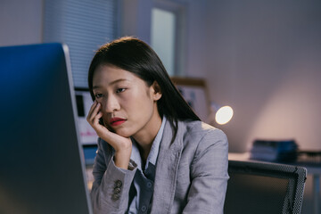 Young professional woman is having problems at work while using desktop computer in dark office at...