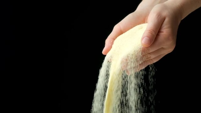 Hands pouring dry semolina durum flour, black background, copy space for text, slow motion