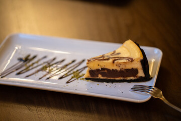 A slice of cheesecake with chocolate filling on a white plate. Cheesecake presentation.