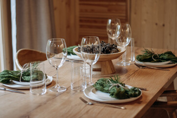 Christmas table setting featuring a fir branches, a cones, a green napkins against the background of a wooden table.