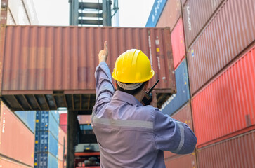 Loading foreman in yellow helmet directing crane operator to lift shipping container at shipyard....