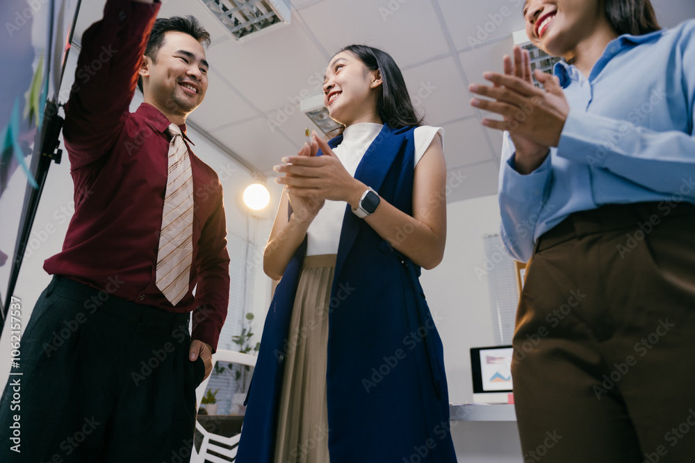Poster enthusiastic business team applauding a colleague explaining a project on a whiteboard during a prod