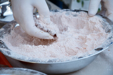A hand is coating the fish roe in flour mixed with paprika in a metal bowl, preparing it for frying.