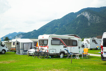 A peaceful scene at a campsite in Wolfgang am See, Austria. Campervans and motorhomes parked and surrounded by lush greenery and mountains in the background.