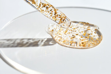 Luxurious skincare serum with golden particles in glass dropper on clear surface against light background