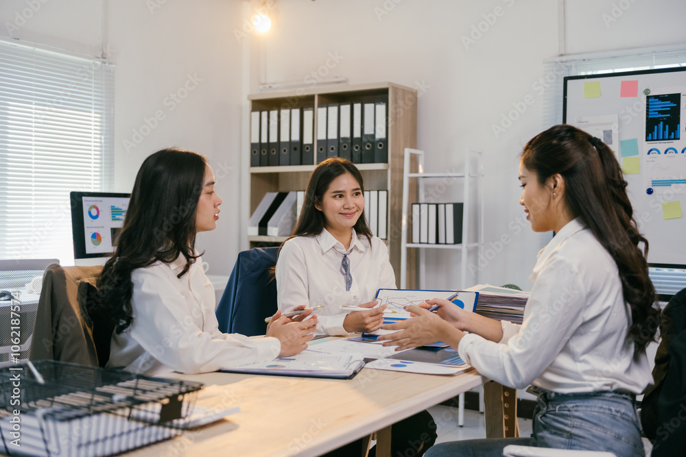 Poster three asian businesswomen are sitting at a table in a modern office, collaborating on a project and 