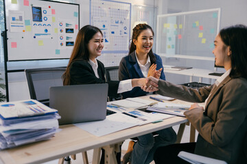 Group of asian businesswomen shaking hands over a desk in a modern office, celebrating a successful agreement or partnership