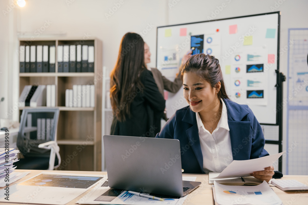 Poster smiling businesswoman uses laptop with colleagues discussing charts in office meeting, showcasing te