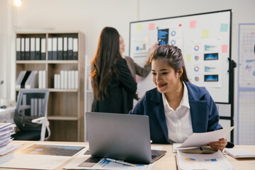 Smiling businesswoman uses laptop with colleagues discussing charts in office meeting, showcasing teamwork and data analysis