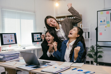 Three euphoric businesswomen are celebrating a successful business achievement in their modern office, expressing joy and teamwork