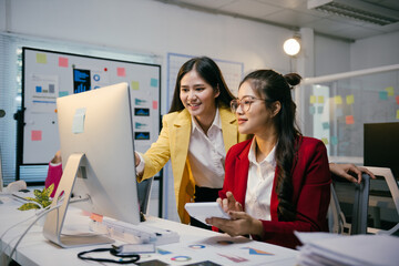 Two young businesswomen collaborating on a project with a computer and calculator in a modern office, showing teamwork and efficiency