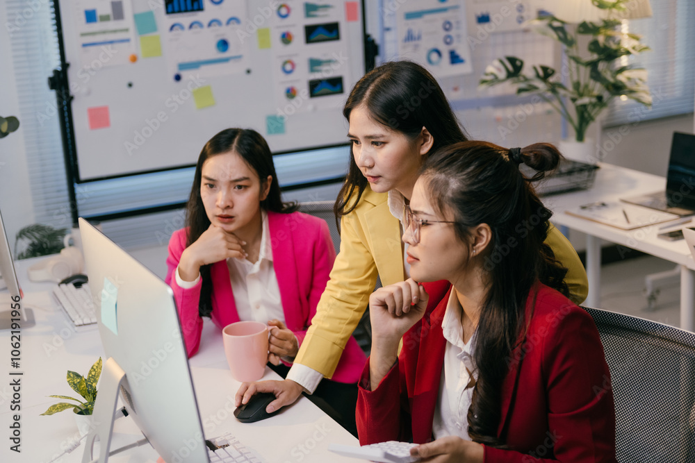 Aufkleber Three asian businesswomen are collaborating on a project, analyzing charts and data displayed on a desktop computer in a modern office environment, demonstrating teamwork and problem-solving skills