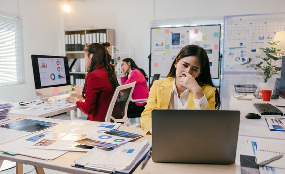 Young asian businesswoman is having problems and feeling stressed at work while sitting at her desk with a laptop and documents in the office - Powered by Adobe