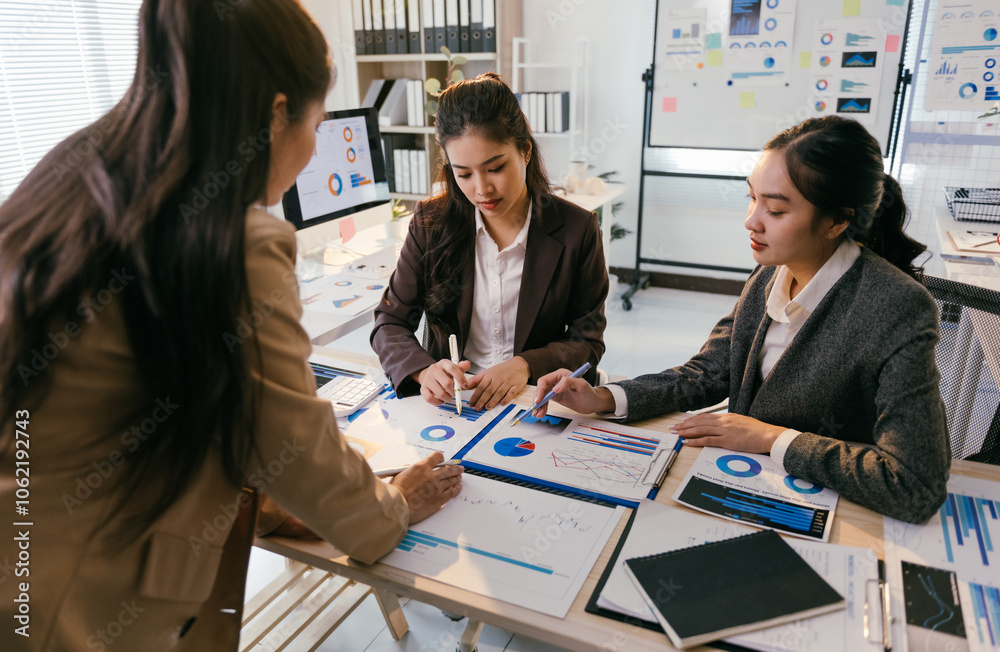 Poster three asian businesswomen are discussing and analyzing financial charts and graphs during a producti