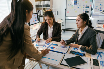 Three asian businesswomen are having a meeting in a modern office, analyzing financial charts and discussing business strategies