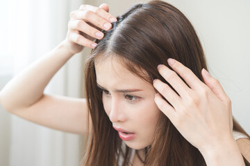 Fototapeta premium Damaged hair symptom, problem hair fall asian young woman, girl worry about balding, looking at scalp in mirror, hand in break into front hair loss, thin problem. Health care treatment for beauty.