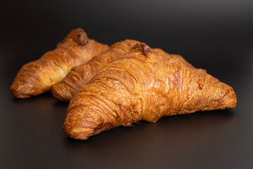 French croissants lying on a black background, golden color shimmering under the spotlight.