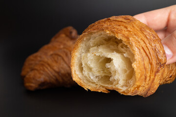 One hand of a girl holds a delicate half of a French croissant, while a full croissant is set against the black background behind her.