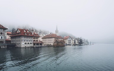 Fototapeta premium A foggy morning view of a lakeside town with traditional architecture.